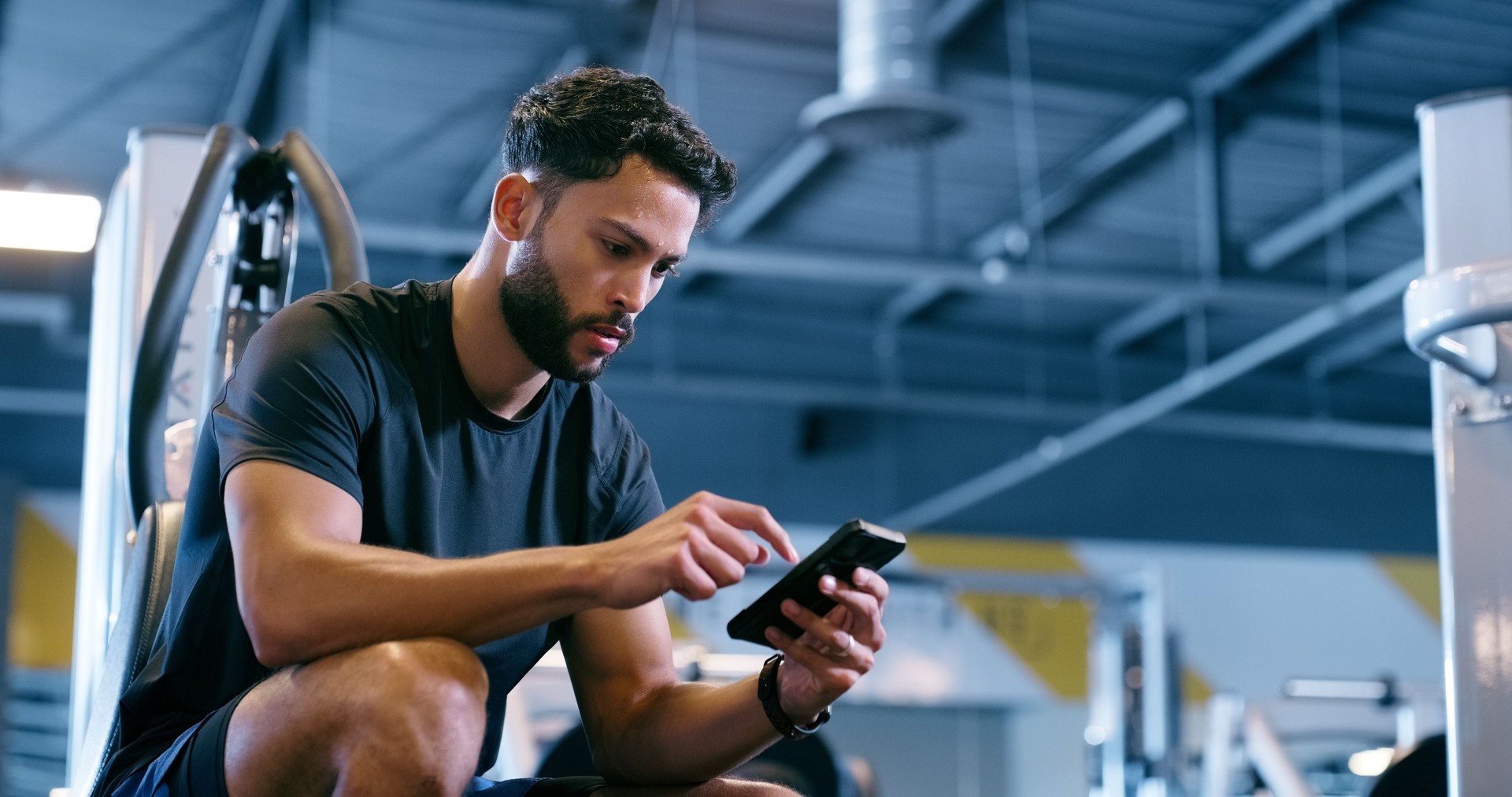 Fitness, cellphone and man in gym, typing and contact with digital app, online reading and internet. Person, health and guy in wellness center, relax and social media with goals and checking progress